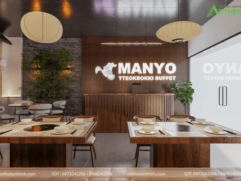 Quầy lễ tân ấn tượng – logo MANYO LED nổi trên vách lam gỗ, đèn lồng giấy lớn, mảng đá tự nhiên trồng tre xanh, dãy bàn lẩu gỗ phía trước